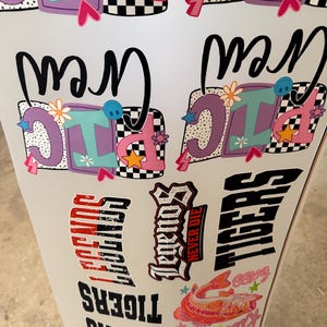 May include: A sheet of assorted vinyl decals featuring colorful designs including the text Picnic Crew in purple and pink, the word Legends in black and red, the word Tigers in black, and a graphic of a fish with the text Kiss My Bass.