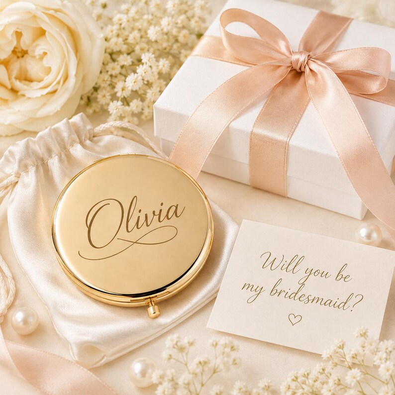 Pu&ograve; includere: Uno specchietto da borsa rotondo color oro inciso con il nome Olivia in corsivo. Lo specchio &egrave; appoggiato su un sacchetto di raso bianco con coulisse accanto a una scatola regalo bianca legata con un nastro color pesca e un biglietto con la scritta Will you be my bridesmaid?