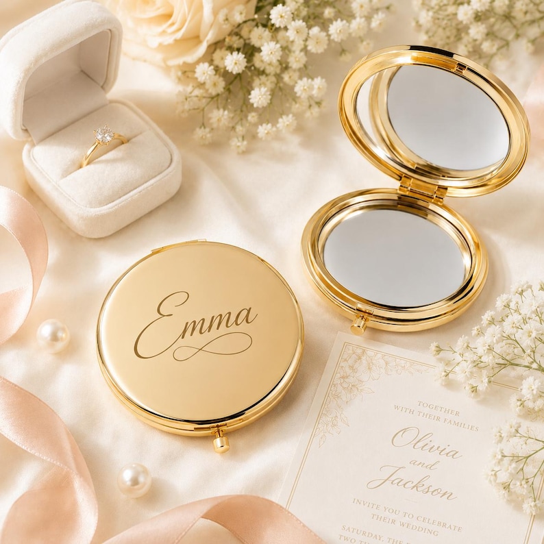 Pu&ograve; includere: Uno specchietto da borsa circolare color oro con il nome Emma inciso in corsivo sul coperchio, accanto a uno specchietto aperto che mostra due superfici riflettenti e un cofanetto bianco contenente un anello dorato con una pietra chiara.