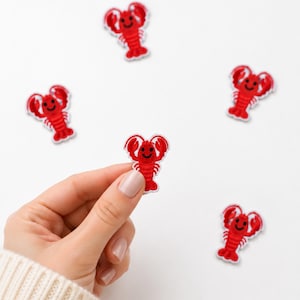 May include: Five small, red embroidered lobster patches with white borders and black stitched facial features. Each lobster has two raised claws, a segmented body, and a smiling expression. The patches are arranged in a scattered pattern.