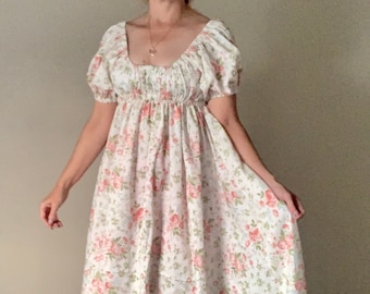 May include: A white maxi dress with a floral print featuring pink roses. The dress has a square neckline, short puff sleeves, and a fitted bodice. The skirt is full and flowing.