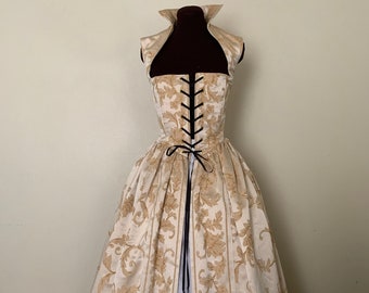 May include: A white and gold brocade gown with a black lace-up bodice and a black ribbon sash. The gown has a high neckline and a fitted bodice. The skirt is full and flowing.