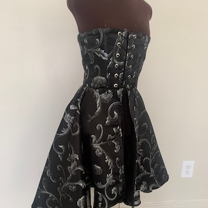 May include: A black strapless dress with a silver floral pattern. The dress has a fitted bodice with a lace-up back and a flowing skirt.