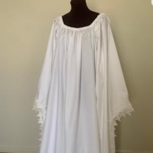 May include: A long, white medieval-style dress with a square neckline and long, flowing sleeves. The sleeves are trimmed with delicate lace. The dress is displayed on a mannequin.