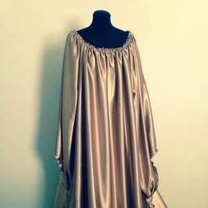 May include: A long, flowing, gold satin gown with a gathered neckline and long sleeves. The sleeves are gathered at the wrists and tied with a bow.