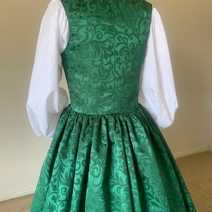 Puede incluir: Un vestido verde con cuello alto y estampado floral. El vestido tiene una falda completa y est&aacute; hecho de una tela sedosa.