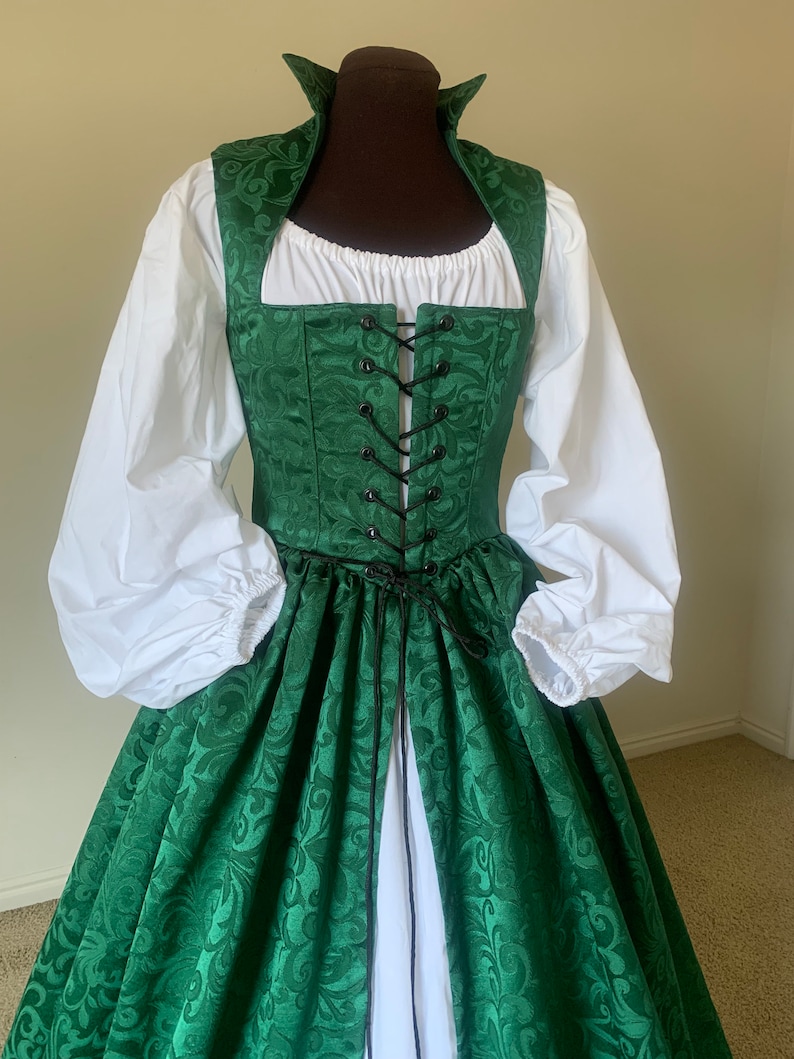 Puede incluir: Un vestido verde y blanco con un corpi&ntilde;o con cordones y una falda completa. El vestido tiene un estampado floral y un cuello alto.