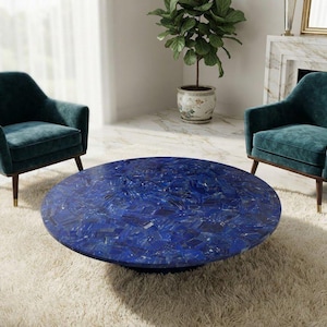 May include: A round coffee table with a vibrant blue mosaic stone top and a low base, positioned between two teal upholstered armchairs with dark wooden legs. The table surface features a textured, fragmented pattern of deep blue mineral pieces.