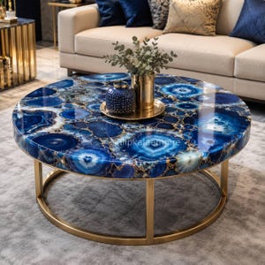 May include: A round coffee table with a polished blue agate top and gold-colored metal base. The table features a glossy surface with intricate blue and white patterns. Decorative vases and a tray are on the table.