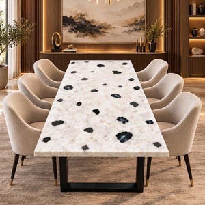 May include: A rectangular dining table featuring a white, semi-translucent stone surface with scattered black, irregular-shaped inclusions. The table is supported by a black metal frame and is surrounded by six beige upholstered dining chairs.