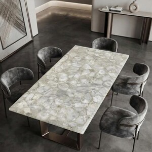 May include: A rectangular dining table featuring a light gray, multi-faceted stone slab top with a polished finish, supported by a dark metal base. The table is surrounded by five curved, gray upholstered chairs with dark metal frames.