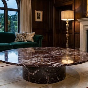 May include: An opulent living room with a circular marble coffee table as the focal point. A dark green velvet sofa with patterned cushions is positioned near a large window. A floor lamp and fireplace add to the room's elegance.