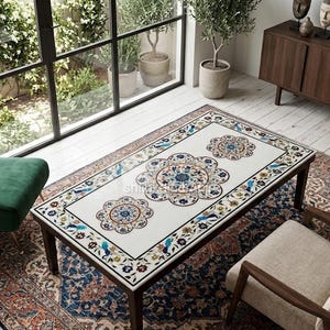 Könnte beinhalten: Ein rechteckiger Couchtisch mit weißer Tischplatte, die mit drei detaillierten floralen Mandalamustern in Blau, Orange und Grün verziert ist. Der Tisch hat einen Rahmen und vier Beine aus dunklem Holz und steht auf einem gemusterten Teppich.