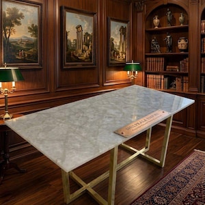 May include: A rectangular table with a polished white translucent stone top and a gold-toned metal base featuring an X-shaped frame. A rectangular plaque with the text SHILPKALA EMPIRE is placed on the surface of the table.