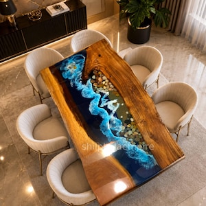May include: A rectangular wooden dining table with a blue resin river design, featuring a wave-like pattern and embedded stones. The table is surrounded by six cream-colored chairs with gold legs, creating a modern dining set.