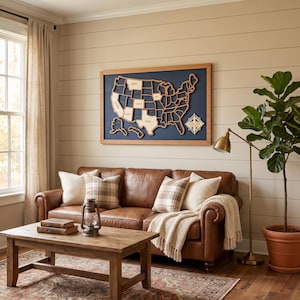 Puede incluir: Un cuadro rectangular que presenta un mapa de madera de los Estados Unidos sobre un fondo azul oscuro, enmarcado en madera clara. El mapa incluye formas de estados recortadas y una rosa de los vientos en la esquina inferior con el texto NEVER STOP EXPLORING.