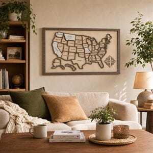 May include: A rectangular wall art piece featuring a wooden map of the United States of America with raised borders for each state, mounted within a dark wood frame. The map includes a compass rose design in the lower right corner with text.