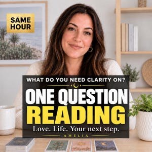 May include: A person with long brown hair sits behind a table with three tarot cards and a deck of cards. A black sign with yellow and white text reads: WHAT DO YOU NEED CLARITY ON? ONE QUESTION READING Love. Life. Your next step. AMELIA.