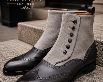 Puede incluir: Un par de botines con puntera de cuero negro estilo wingtip y contrafuerte con detalles brogue. La caña es de ante gris e incluye un cierre lateral con seis botones negros. El texto HS HANDSHAPED LEATHER es visible en la imagen.