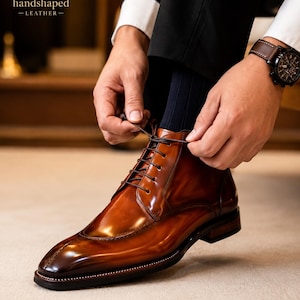 Può includere: Uno stivaletto in pelle color marrone cognac lucido con punta arrotondata, lacci marrone scuro e una cucitura a vista sul guardolo. Lo stivale presenta una finitura liscia e lucida e un tacco a strati marrone scuro. Il logo HS handshaped LEATHER è visibile.