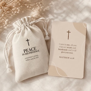 May include: A beige drawstring fabric pouch printed with a cross and the text PEACE IN HIS PRESENCE a moment to pause, reflect and be still, alongside a rectangular card featuring a cross and the text Matthew 11:28 Come to me, all you who are weary and burdened, and I will give you rest.