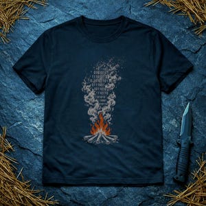 May include: A dark navy blue short-sleeve t-shirt featuring a graphic print of a campfire with logs at the base and orange flames. Rising from the fire is a plume of grey smoke that incorporates a pattern of binary code digits in white.