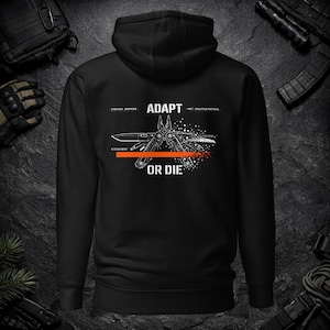 May include: A black hooded sweatshirt featuring a white graphic on the back. The design displays a multi-tool illustration with the text ADAPT OR DIE, binary code, and a horizontal orange line. The graphic includes small scattered white dots.