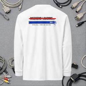 Op de afbeelding: Een wit shirt met lange mouwen en een afbeelding op de achterkant. Het ontwerp bevat de tekst "WEEKEND LOADING..." met een rode streep erdoor, een blauwe voortgangsbalk op 99% en de tekst "SYSTEM_STALL // ERROR_CODE: 0x99_FATAL".