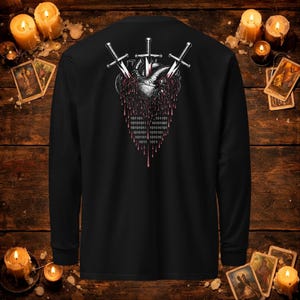 May include: A black long-sleeve shirt featuring a graphic on the back of an anatomical heart pierced by three silver swords. The heart appears to be dripping red liquid, and the lower portion of the design contains binary code in white text.