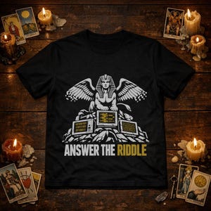 May include: Black t-shirt with a white and gold graphic of a winged sphinx above computer monitors displaying binary code. The text "ANSWER THE RIDDLE" is printed in gold below the graphic. The design is set against a dark background.