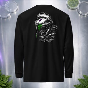 Puede incluir: Una camiseta negra de manga larga con un estampado gráfico blanco de una planta carnívora Venus atrapamoscas con un ratón de ordenador en sus fauces. La planta tiene dientes afilados y baba verde que gotea, con un cable colgando del ratón.