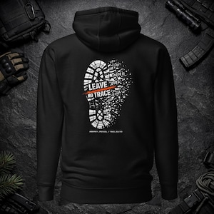 Puede incluir: Una sudadera con capucha negra con un gráfico blanco en la espalda. El diseño muestra una huella de bota disolviéndose en código binario con una línea horizontal naranja y el texto LEAVE NO TRACE y ANONYMITY_PROTOCOL // TRACE_DELETED.