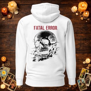 May include: A white hooded sweatshirt featuring a black graphic of a human skull with a digital glitch effect across the centre. Above the skull, the text FATAL ERROR is printed in a distressed red font. The hoodie has long sleeves and a hood.