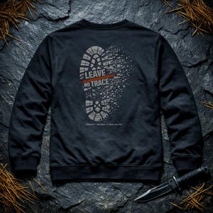 May include: Black crew neck sweatshirt featuring a grey boot print design. The design includes the words "LEAVE NO TRACE" with a red line through it, and binary code. A black knife is in the bottom right corner.