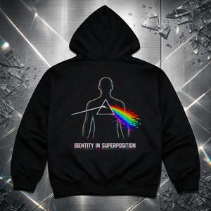 Puede incluir: Una sudadera negra con capucha y un gráfico en la parte posterior. El diseño muestra el contorno de una silueta humana con un prisma triangular central que refracta un rayo blanco en un espectro de arcoíris pixelado. Dice IDENTITY IN SUPERPOSITION.