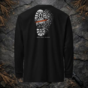 May include: A black long-sleeve shirt featuring a white graphic on the back of a boot print dissolving into binary code. The design includes the text "LEAVE NO TRACE" in white with an orange horizontal line, and "ANONYMITY_PROTOCOL // TRACE_DELETED" below.