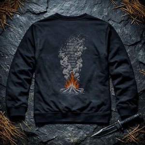 Puede incluir: Una sudadera negra de manga larga con un estampado gráfico en la espalda. El diseño muestra una fogata con llamas naranjas y rojas, con humo gris ascendente. El humo está compuesto por código binario de unos y ceros.