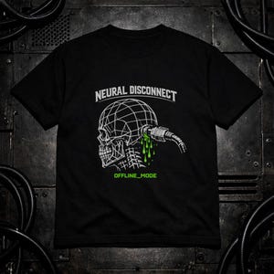 Può includere: T-shirt nero con grafica bianca di un teschio a filo con una spina e liquido verde gocciolante. Il testo "NEURAL DISCONNECT" è sopra il teschio e "OFFLINE_MODE" sotto.