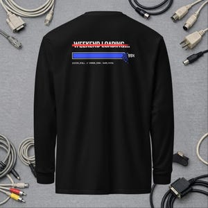 May include: A black long-sleeve shirt featuring a graphic on the back that reads WEEKEND LOADING with a red line through it, a blue progress bar at 99 percent, and the text SYSTEM_STALL // ERROR_CODE: 0x99_FATAL printed in white below the bar.