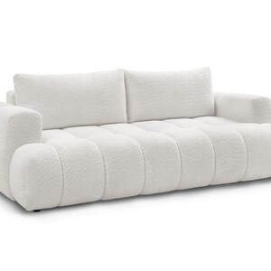 Op de afbeelding: Een witte, pluche bank met een modern design. De bank heeft een gecapitonneerde zitting en rugleuning, met twee grote rugkussens en afgeronde armleuningen. De stof heeft een getextureerde, boucl&eacute;-uitstraling.