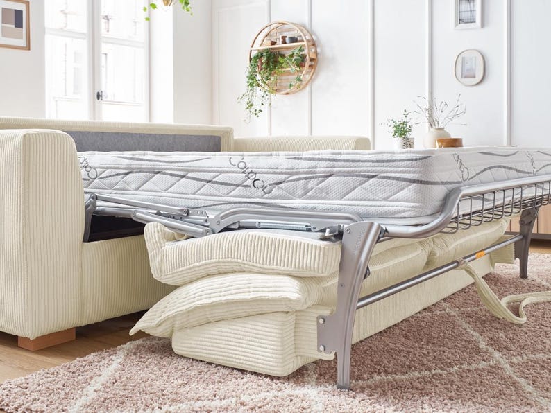 Peut inclure: Un canap&eacute; en velours c&ocirc;tel&eacute; beige avec un cadre de lit gigogne. Le matelas est blanc avec un motif gris. Le canap&eacute; a plusieurs coussins cr&egrave;me et repose sur un tapis brun clair. Le cadre du lit est argent&eacute;.