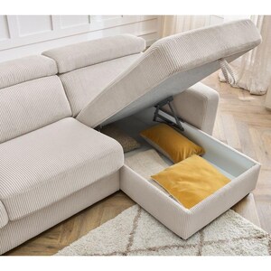 May include: Beige corduroy sectional sofa with an open storage compartment containing two yellow cushions. The sofa sits on a patterned rug. A small side table with a vase of flowers is also visible.