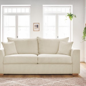 Peut inclure: Un canap&eacute; en velours c&ocirc;tel&eacute; cr&egrave;me avec deux coussins d'assise et quatre coussins assortis. Le canap&eacute; repose sur une base en bois clair. La pi&egrave;ce a deux fen&ecirc;tres et un sch&eacute;ma de couleurs neutres.