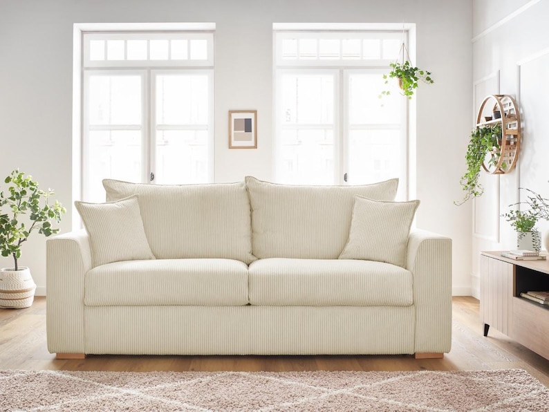 Peut inclure: Un canap&eacute; en velours c&ocirc;tel&eacute; cr&egrave;me avec deux coussins d'assise et quatre coussins assortis. Le canap&eacute; repose sur une base en bois clair. La pi&egrave;ce a deux fen&ecirc;tres et un sch&eacute;ma de couleurs neutres.
