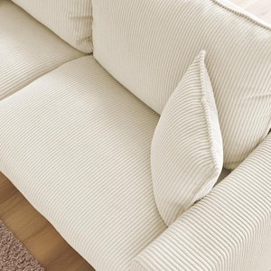 Peut inclure: Gros plan sur un canap&eacute; en velours c&ocirc;tel&eacute; cr&egrave;me avec plusieurs coussins. Le canap&eacute; pr&eacute;sente une texture c&ocirc;tel&eacute;e et une palette de couleurs neutres, adapt&eacute;e &agrave; divers styles de d&eacute;coration int&eacute;rieure. Les coussins sont doux et accueillants.