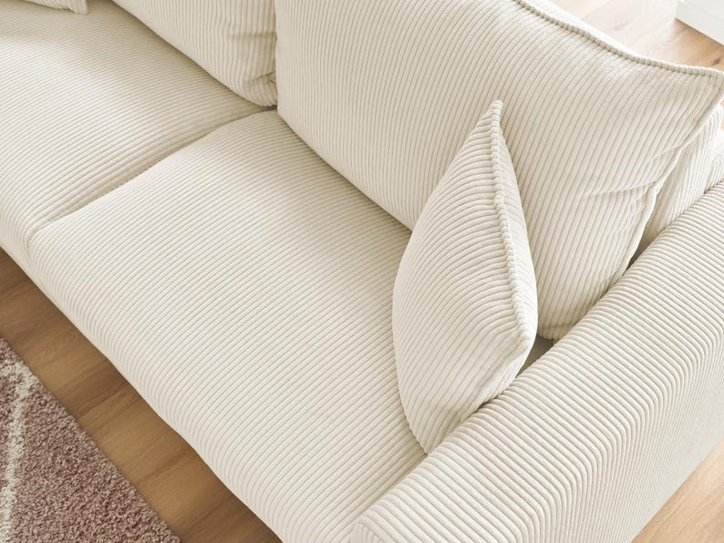 Peut inclure: Gros plan sur un canap&eacute; en velours c&ocirc;tel&eacute; cr&egrave;me avec plusieurs coussins. Le canap&eacute; pr&eacute;sente une texture c&ocirc;tel&eacute;e et une palette de couleurs neutres, adapt&eacute;e &agrave; divers styles de d&eacute;coration int&eacute;rieure. Les coussins sont doux et accueillants.