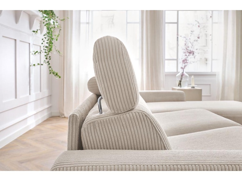 May include: Beige corduroy sectional sofa with adjustable headrests. The sofa has a modern design with a neutral colour palette, suitable for a living room. The headrests are supported by a silver metal frame.