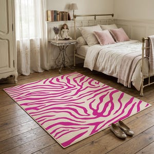 Peut inclure: Un tapis rectangulaire orné d'un motif rayé zébré rose vif et audacieux sur un fond de couleur crème. Le tapis est disposé sur un plancher en bois dans une chambre, mettant en valeur un motif animalier répétitif sur toute sa surface.