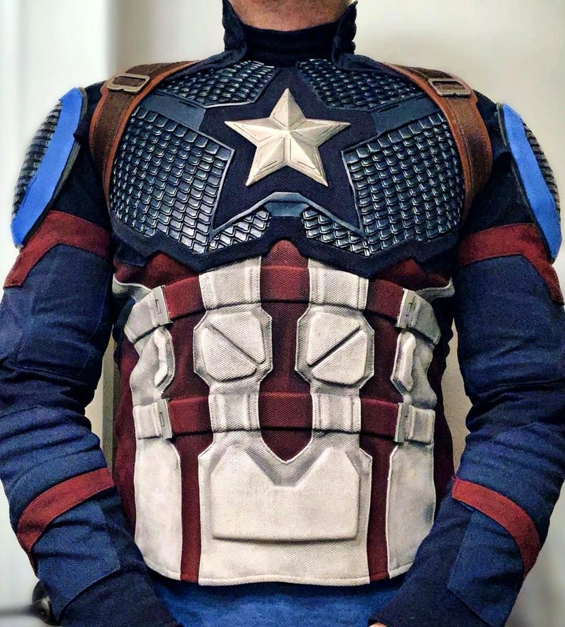 May include: A Captain America costume featuring a navy blue and red color scheme. The chest piece has a silver star and a grid-like pattern. Brown straps cross the shoulders. The costume includes blue sleeves with red accents.