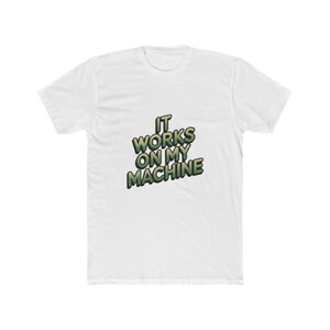 May include: A white short-sleeved t-shirt featuring the text IT WORKS ON MY MACHINE printed in a bold, green-to-yellow gradient font with a dark outline. The lettering is arranged in three lines across the center of the chest area.